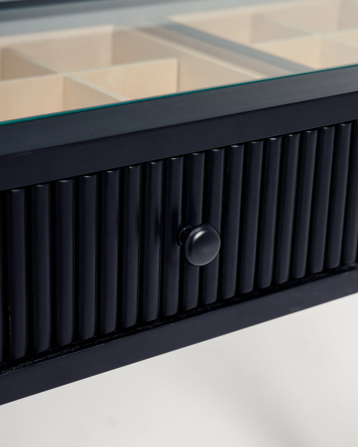 Close-up view of a sleek black dresser drawer featuring a ribbed design and a round black knob. The drawer is partially open, revealing a glass top with compartments inside, ideal for organizing cosmetics or accessories.