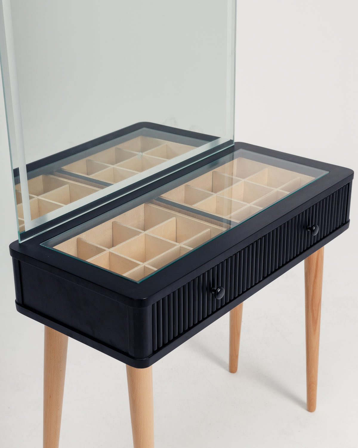 A sleek black vanity table features a large rectangular mirror and a transparent top with multiple compartments underneath for organized storage. The table is supported by stylish wooden legs, enhancing its modern elegance.