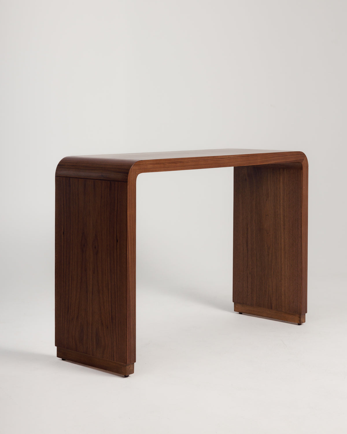 A sleek walnut console table features a smooth, curved design with a rich wood grain finish. The table stands on sturdy rectangular legs, making it an elegant addition to any entryway or living space.