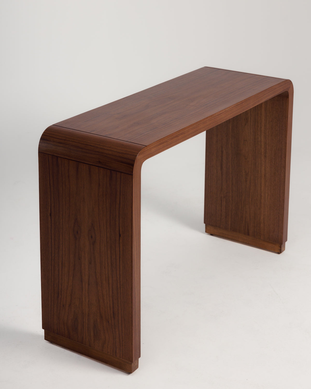 A sleek walnut console table features a smooth, curved design with a rich wood grain finish. Its minimalist style and sturdy construction make it an elegant addition to any entryway or living space.