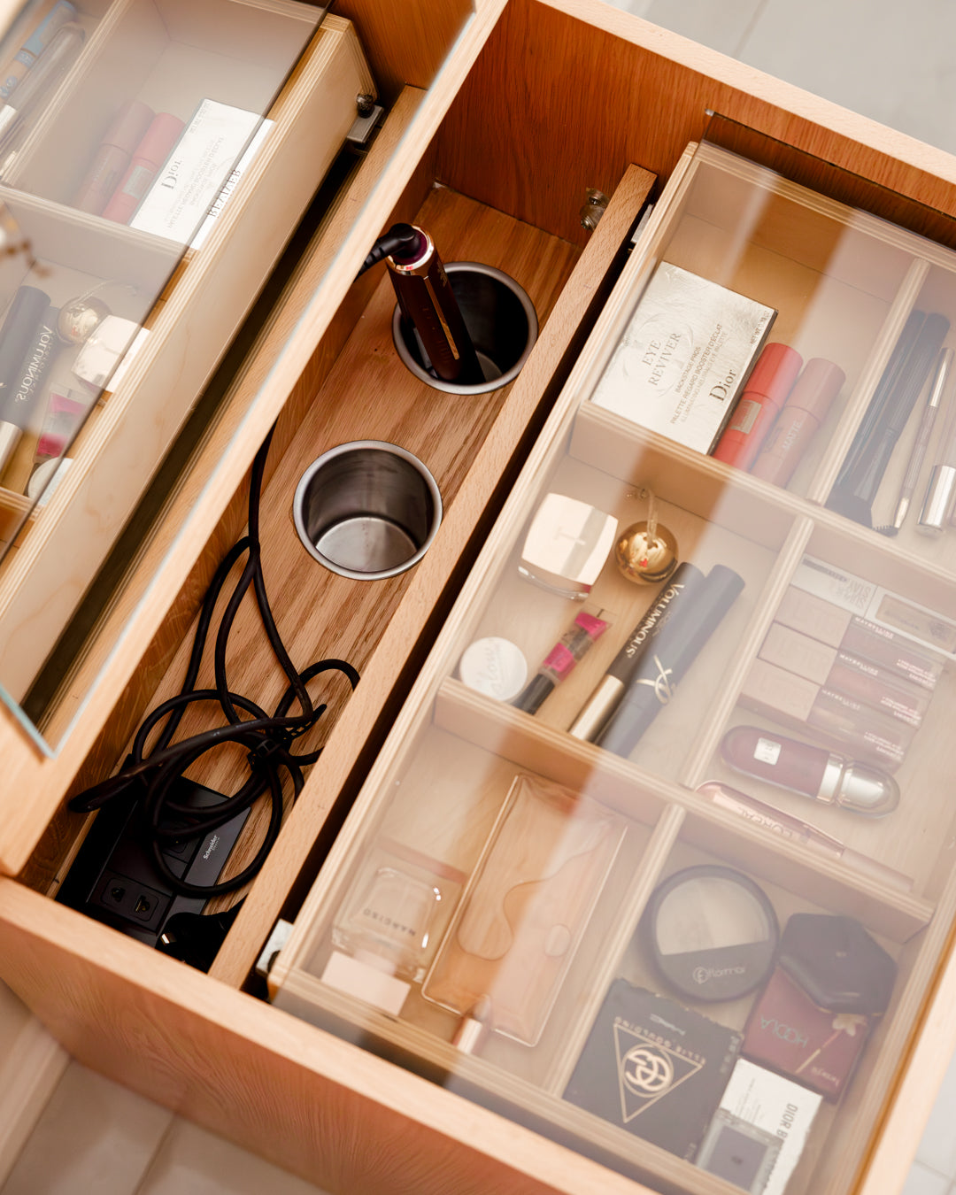 A close-up view of a dresser drawer featuring an organized layout with various makeup items, including lipsticks and skincare products, alongside a circular container for brushes.