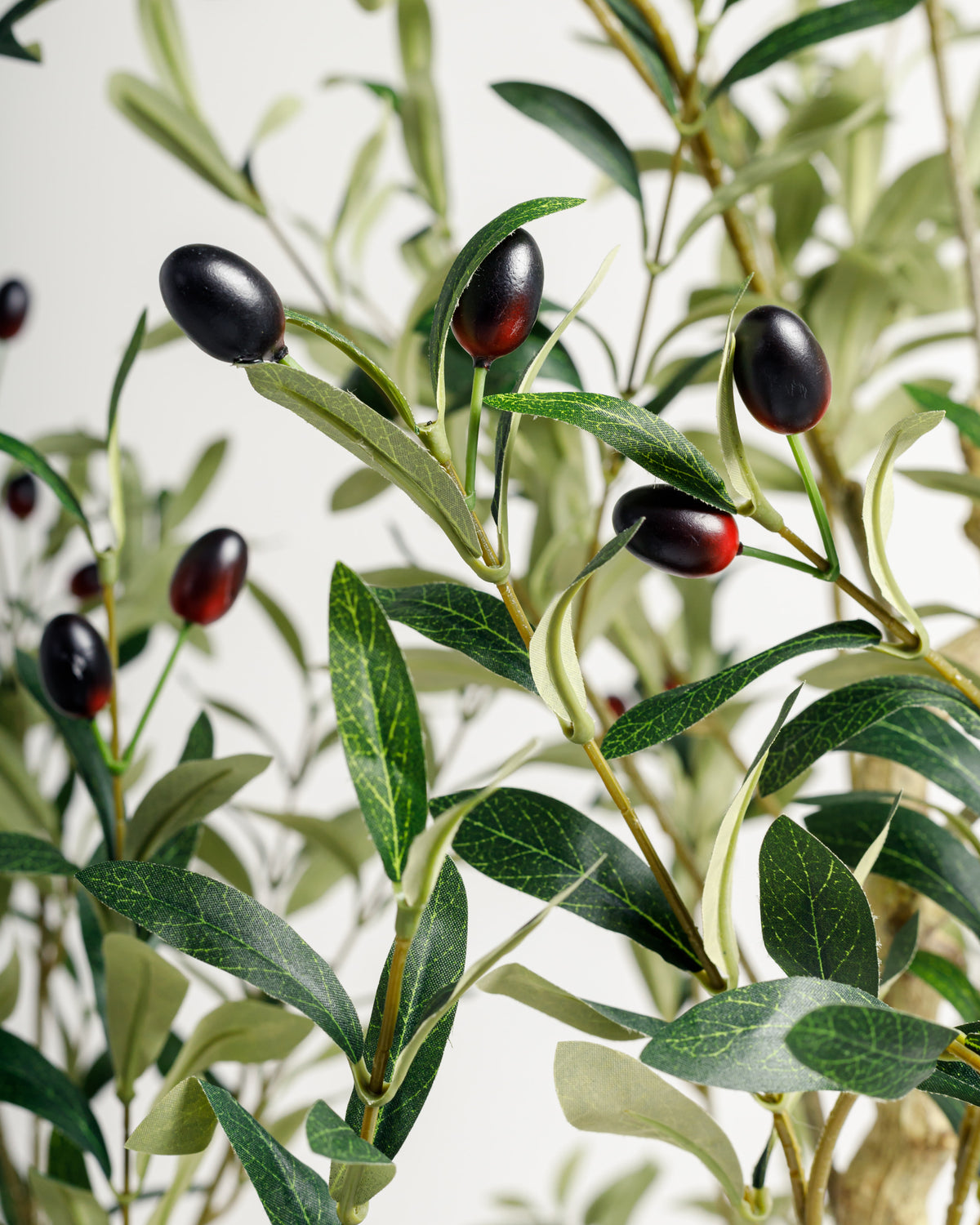 A close-up view of a decorative olive branch featuring realistic green leaves and black olives, highlighting the intricate details of the foliage and fruit. The arrangement showcases a natural look.