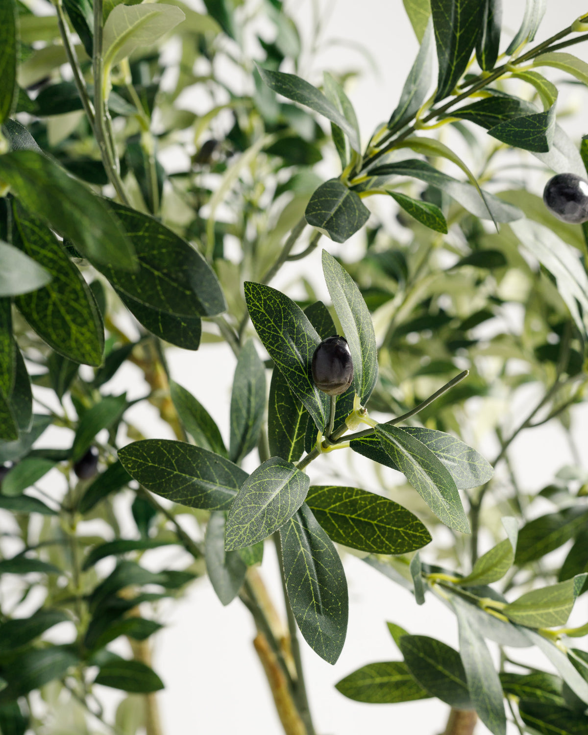 Close-up of a lifelike artificial olive tree, featuring rich green leaves with intricate vein patterns and small black olives. The realistic design adds a touch of natural beauty perfect for enhancing any indoor space.