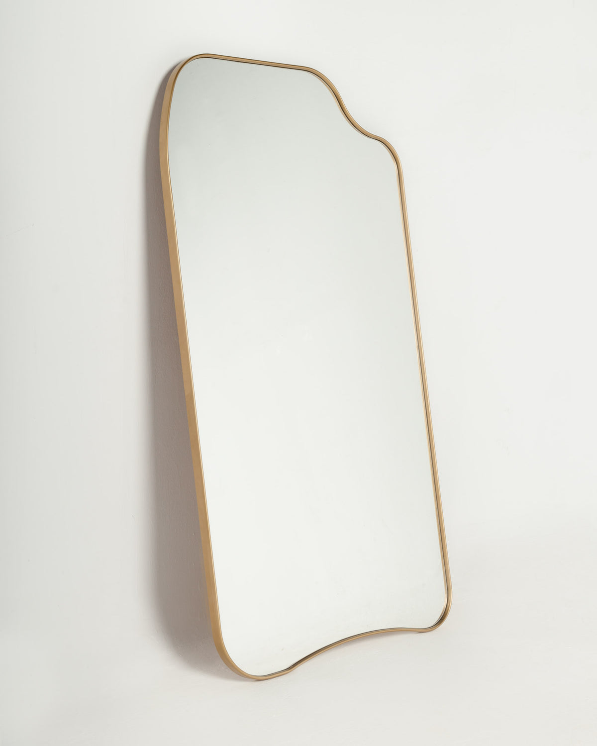 A full-length mirror with a unique, organic shape and a thin gold frame is displayed against a plain white background. The mirrors design adds a modern and stylish touch, reflecting light and enhancing the surrounding space.