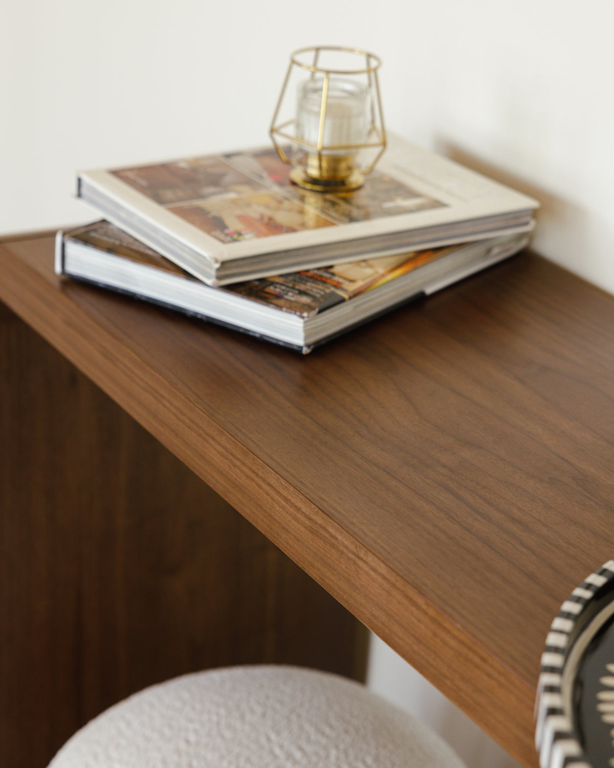 A close-up view of a walnut console table featuring a smooth wooden surface with a rich, warm finish. On top, there are two stacked photo books and a decorative glass candle holder, adding a stylish touch to the tabletop.