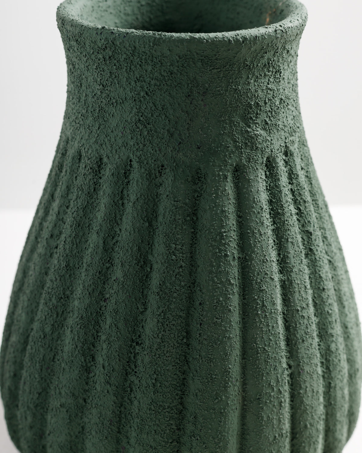 A textured green vase features a ribbed design with a wide opening at the top. The surface has a rough finish, adding a rustic charm to the overall appearance, making it a striking decorative piece.