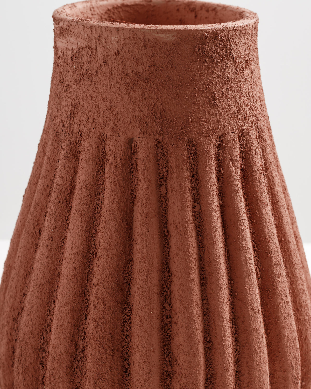 A close-up view of a terracotta vase featuring a textured, ribbed design. The warm, earthy tones of the vase highlight its unique surface, creating a rustic yet modern aesthetic suitable for various decor styles.