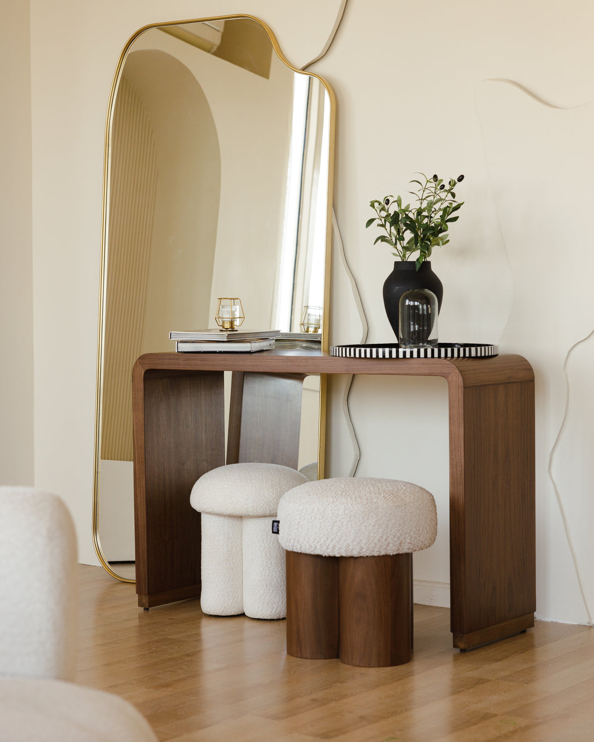 A stylish wooden console table with a curved design holds a decorative vase with greenery and a small stacked book.