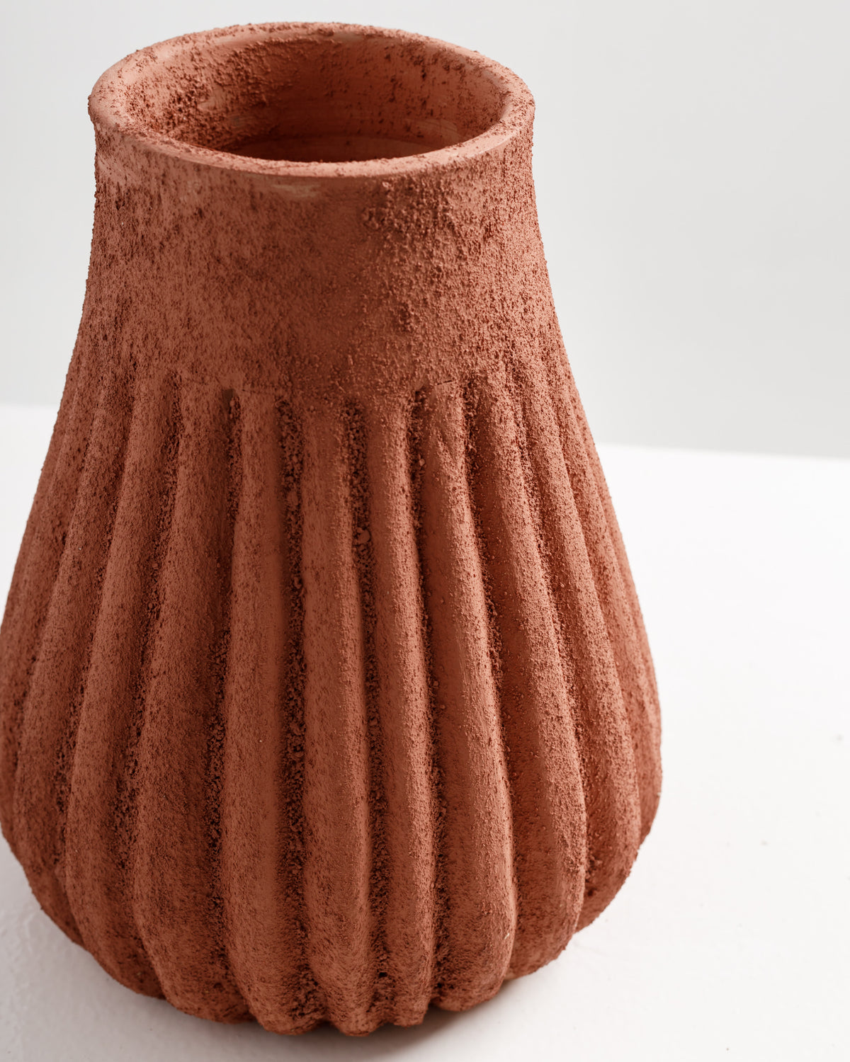 A textured terracotta vase featuring vertical ribbing and a wide opening at the top. The warm, earthy color and rustic finish make it an attractive decorative piece for various settings.