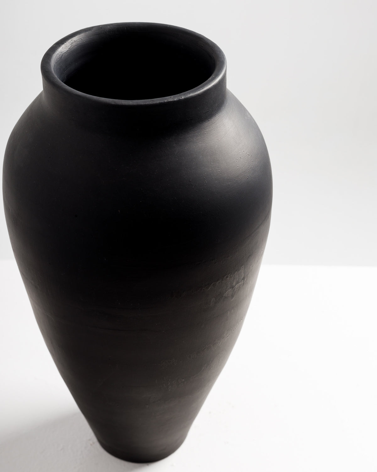 A tall, elegant black vase with a smooth, matte finish is displayed against a light background. Its rounded body tapers towards the base, creating a modern and minimalist aesthetic.