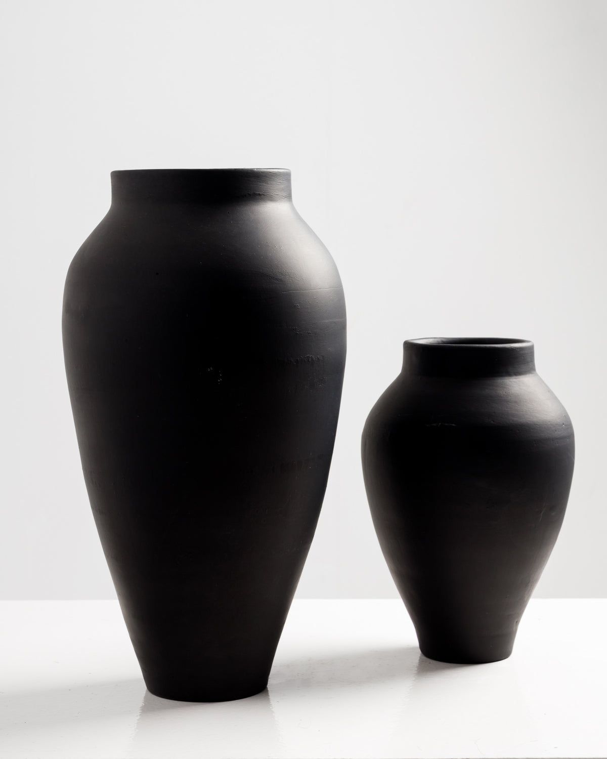 Two elegant black vases in different sizes are displayed against a white background. The larger vase has a rounded silhouette, while the smaller one features a more tapered shape, both showcasing a matte finish that adds a modern touch.
