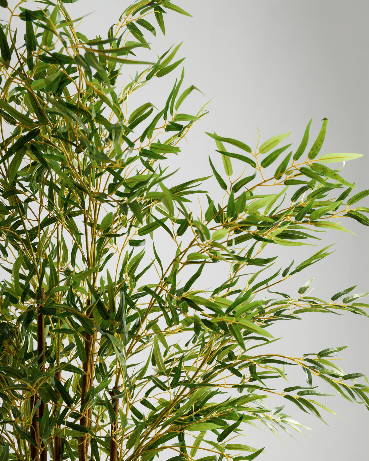 A close-up view of a lush, green bamboo artificial plant with detailed, lifelike leaves. The vibrant greenery creates a tropical ambiance, perfect for enhancing indoor spaces like offices or living rooms.