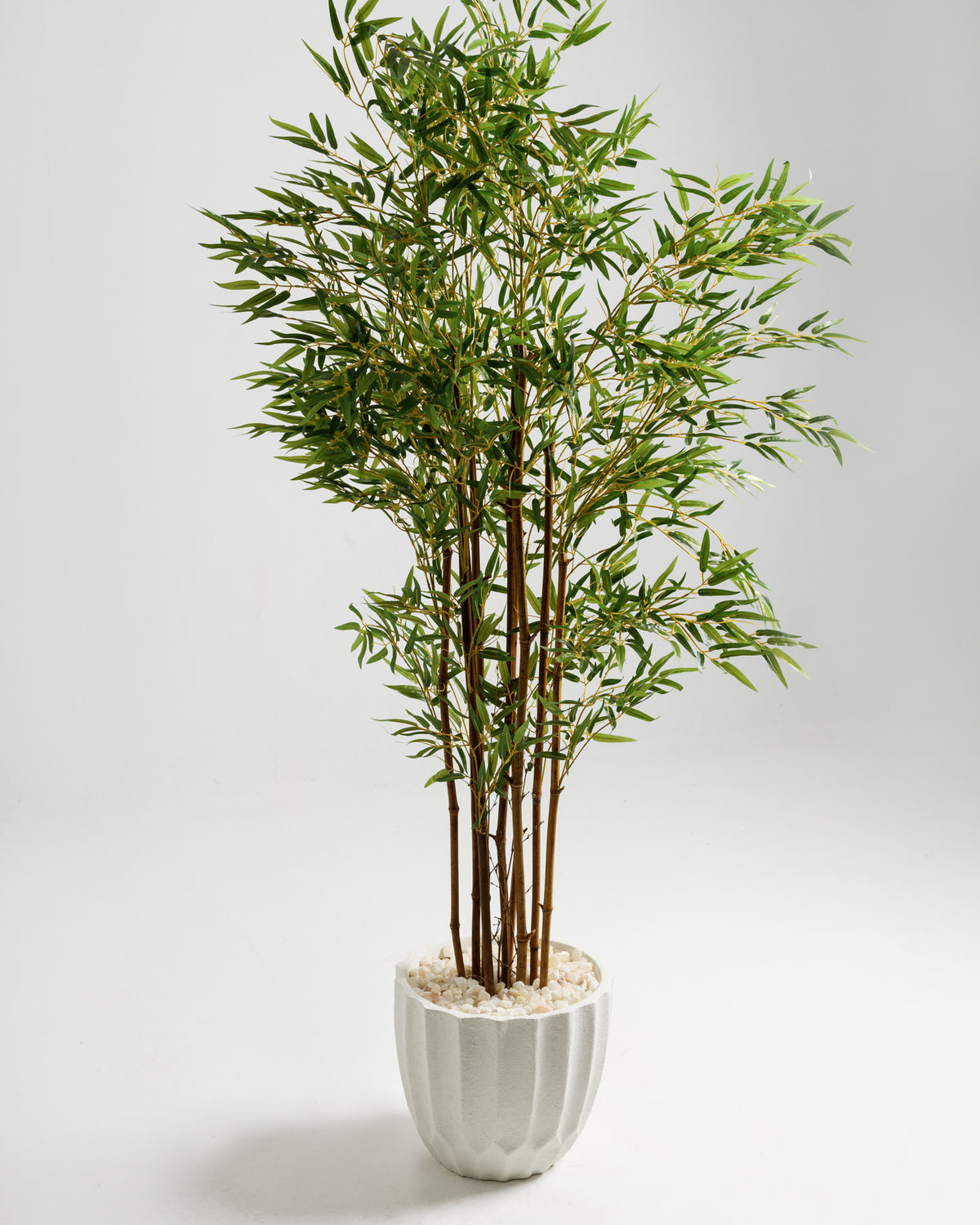 A tall bamboo artificial plant features lush green leaves and multiple slender stems, presented in a textured white pot filled with decorative stones. This elegant piece adds a touch of tropical charm to any indoor space.