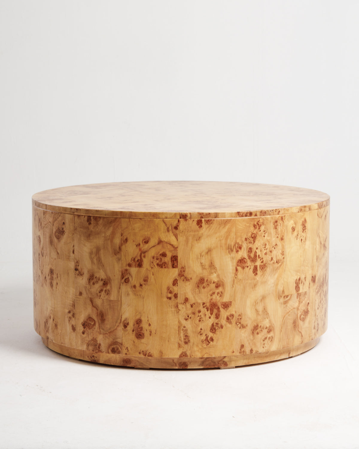 A round coffee table with a burlwood finish, showcasing a smooth surface and intricate wood grain patterns. The table is positioned on a light-colored floor, complementing its natural aesthetic and adding elegance to the room.