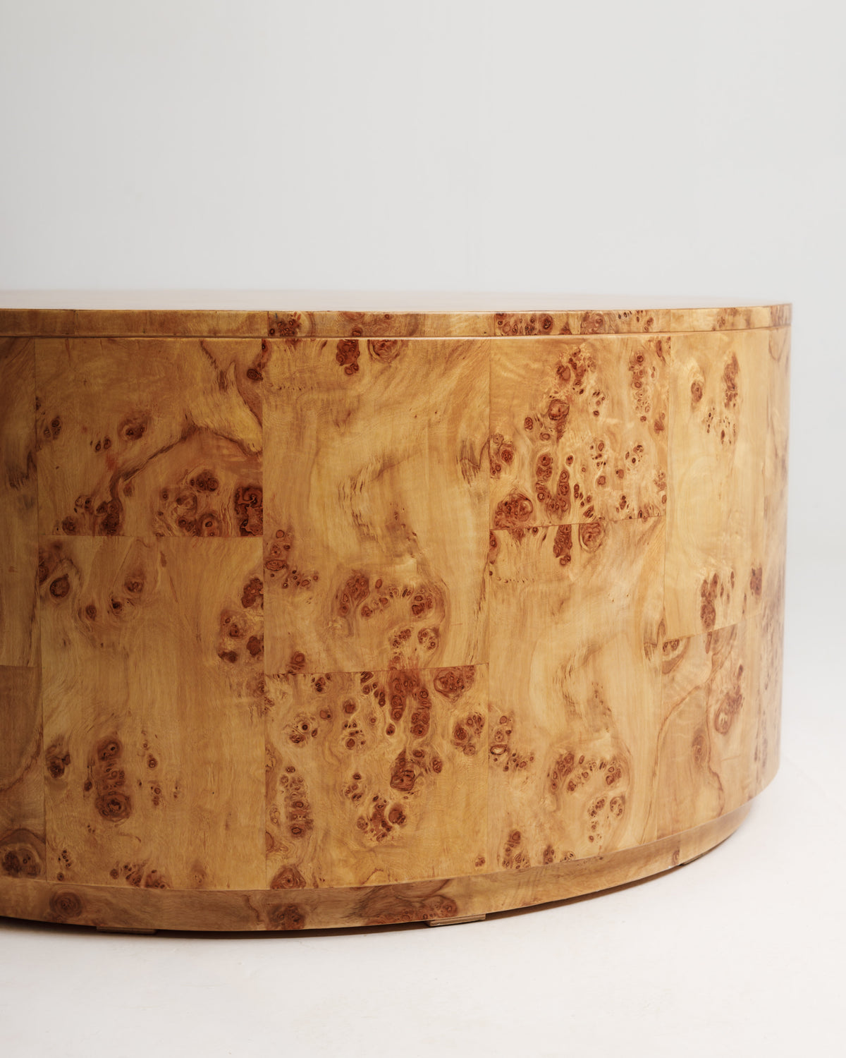 Close-up view of a round coffee table featuring a burlwood finish, showcasing its unique grain patterns and warm tones. The smooth surface and rounded edges create an elegant and modern aesthetic for any living space.