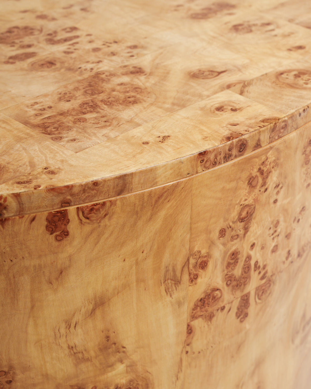 Close-up view of a round coffee table made of burlwood, showcasing its unique, textured surface with intricate patterns and warm.