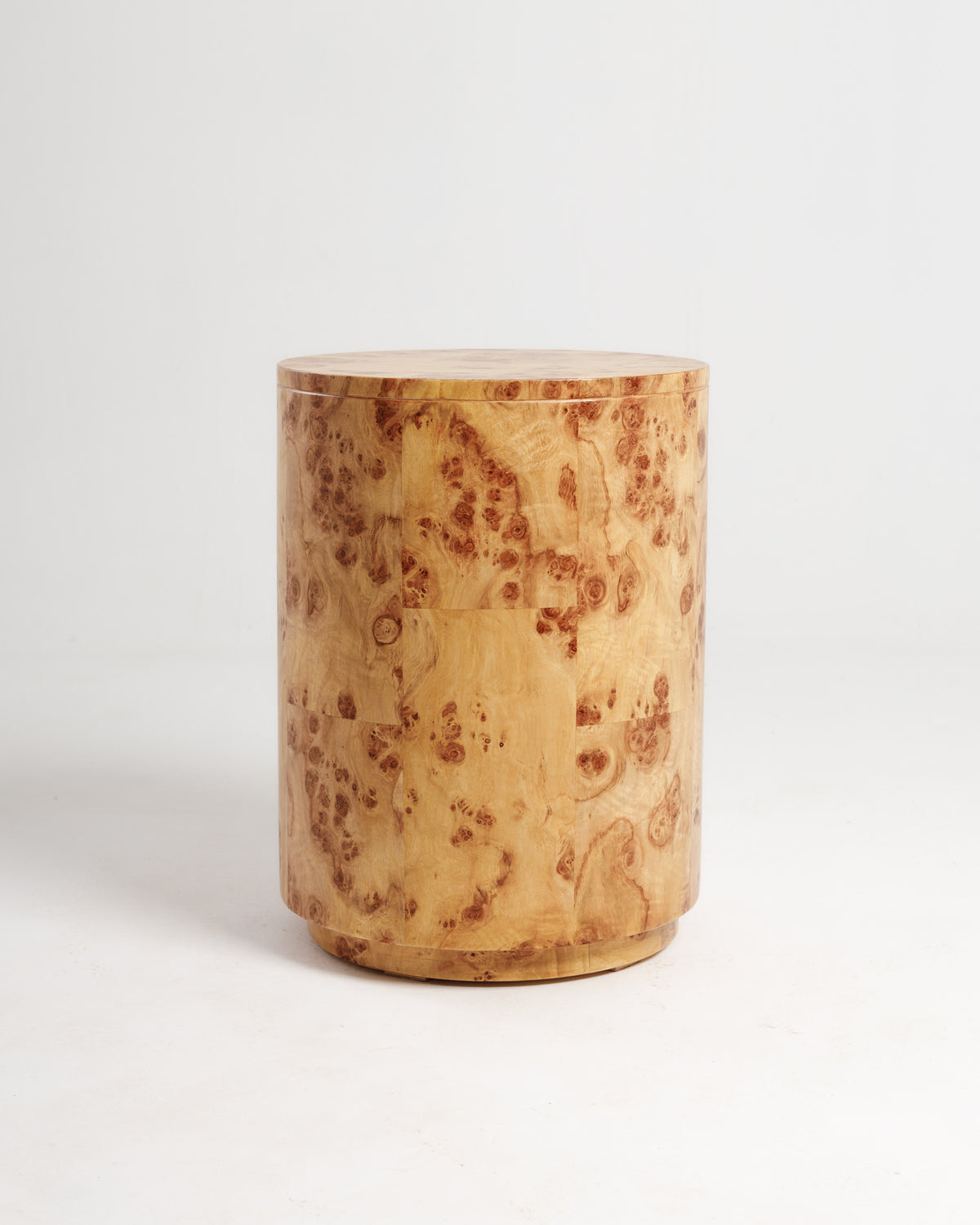 A round side table made of burlwood features a smooth, polished surface and a natural wood grain pattern, showcasing rich tones of light brown with darker swirls.
