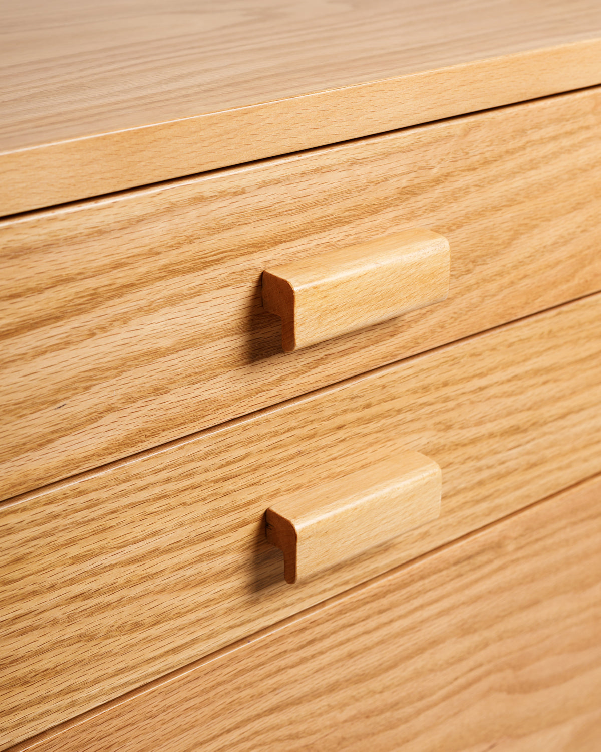 Close-up view of a light wooden dresser featuring two drawers with simple, rectangular wooden handles. The smooth surface and natural grain of the wood add a touch of elegance to the design, making it an appealing storage solution.