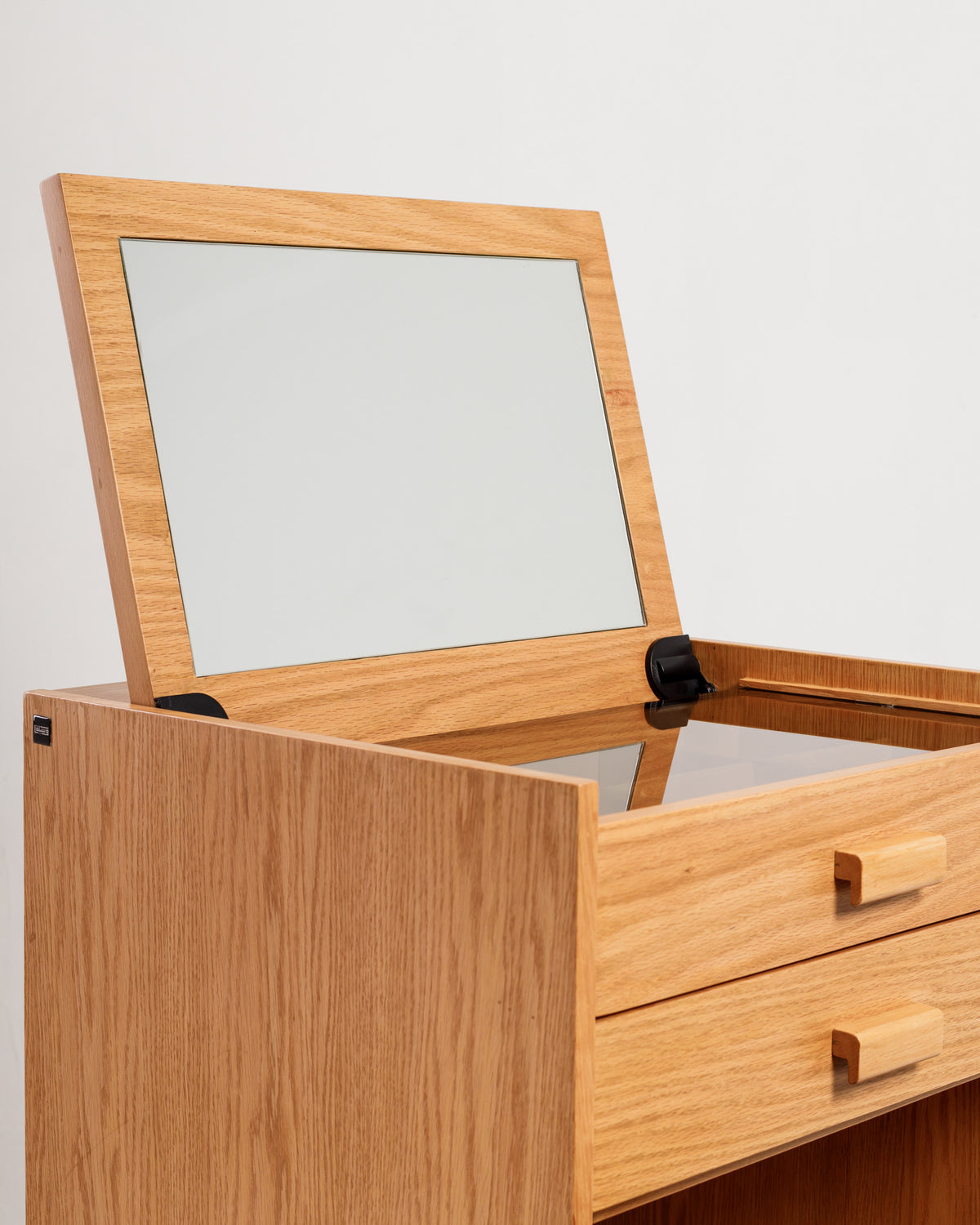 A wooden dresser with a light oak finish features an open top compartment revealing a mirror, designed for easy access while getting ready. The dresser includes two drawers at the front for organized storage of makeup and accessories.