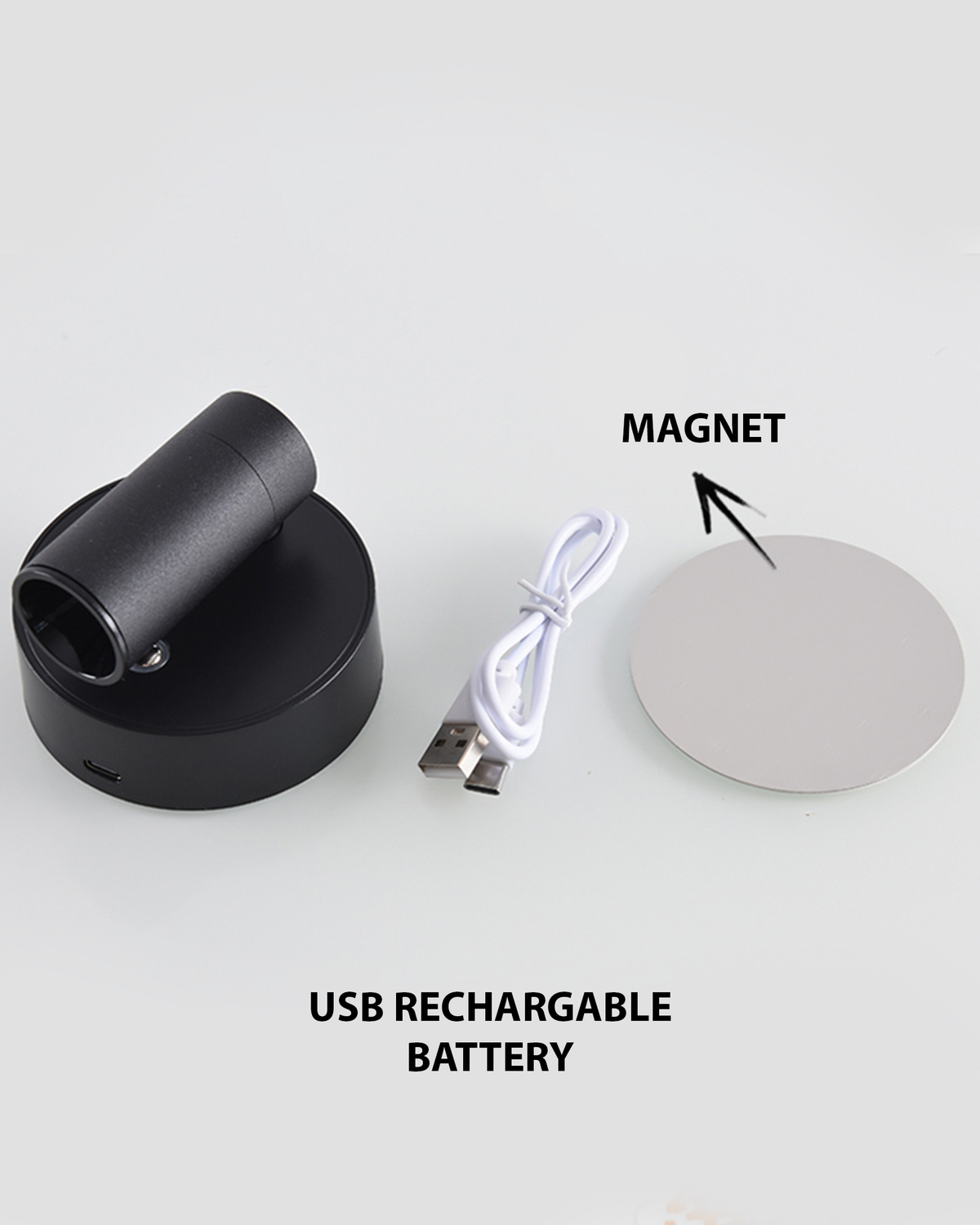 A black rechargeable spotlight with a cylindrical lamp head is positioned on a circular base. Next to it, a USB charging cable and a round magnetic plate are displayed, highlighting the lights wireless and easily mountable features.