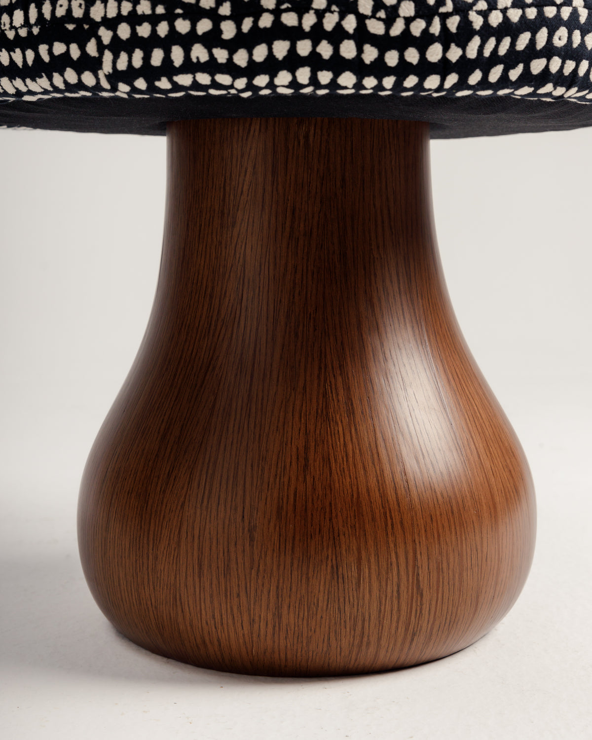 Close-up view of a Mushroom Pouf featuring a sleek, curvaceous wooden base with a rich, dark wood grain. The top showcases a padded cushion with a black and white patterned fabric, emphasizing modern design and organic charm.