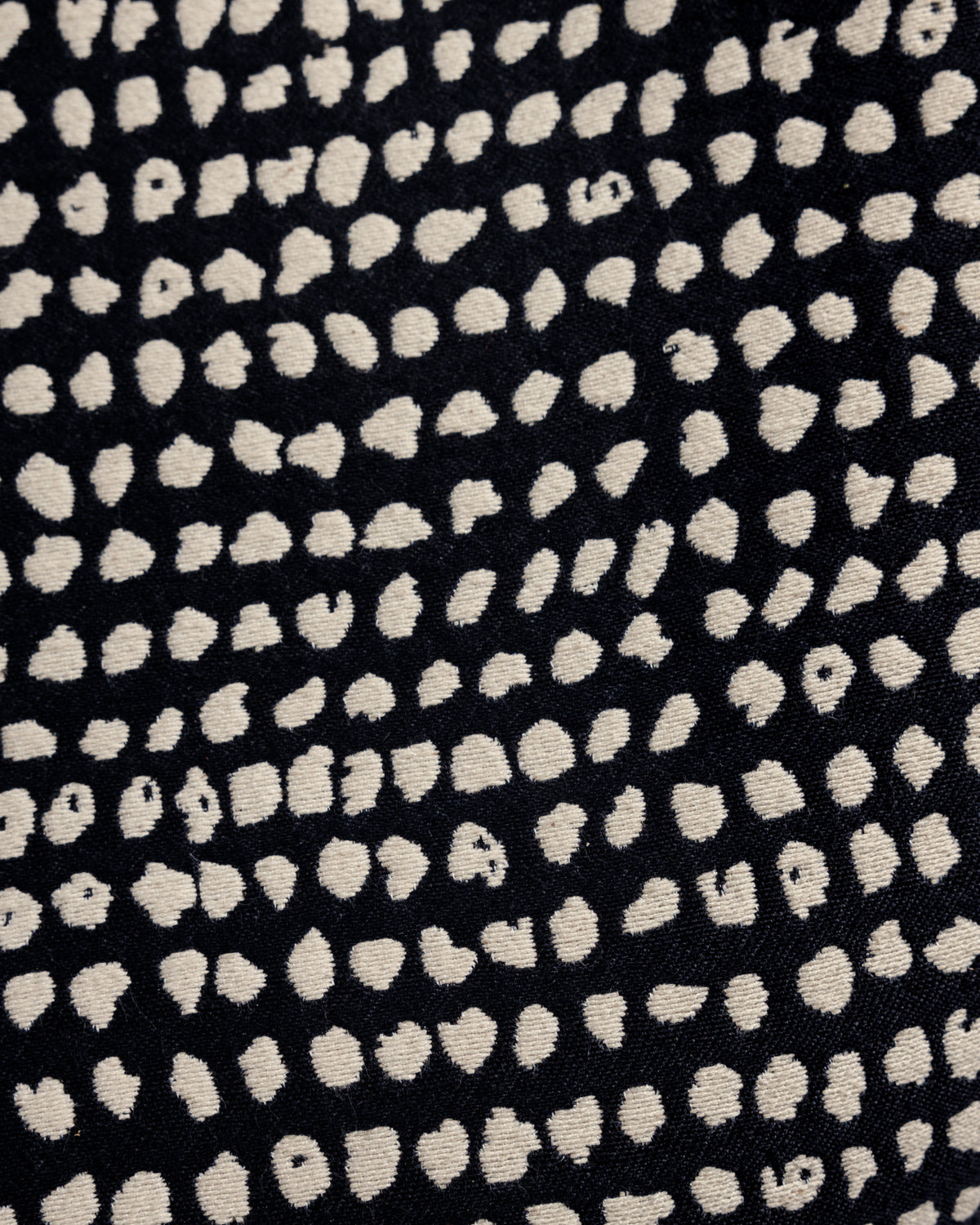 Close-up view of a textured fabric featuring a bold pattern of irregular white dots on a dark background. The design creates a modern and dynamic visual effect, suitable for various home decor applications.