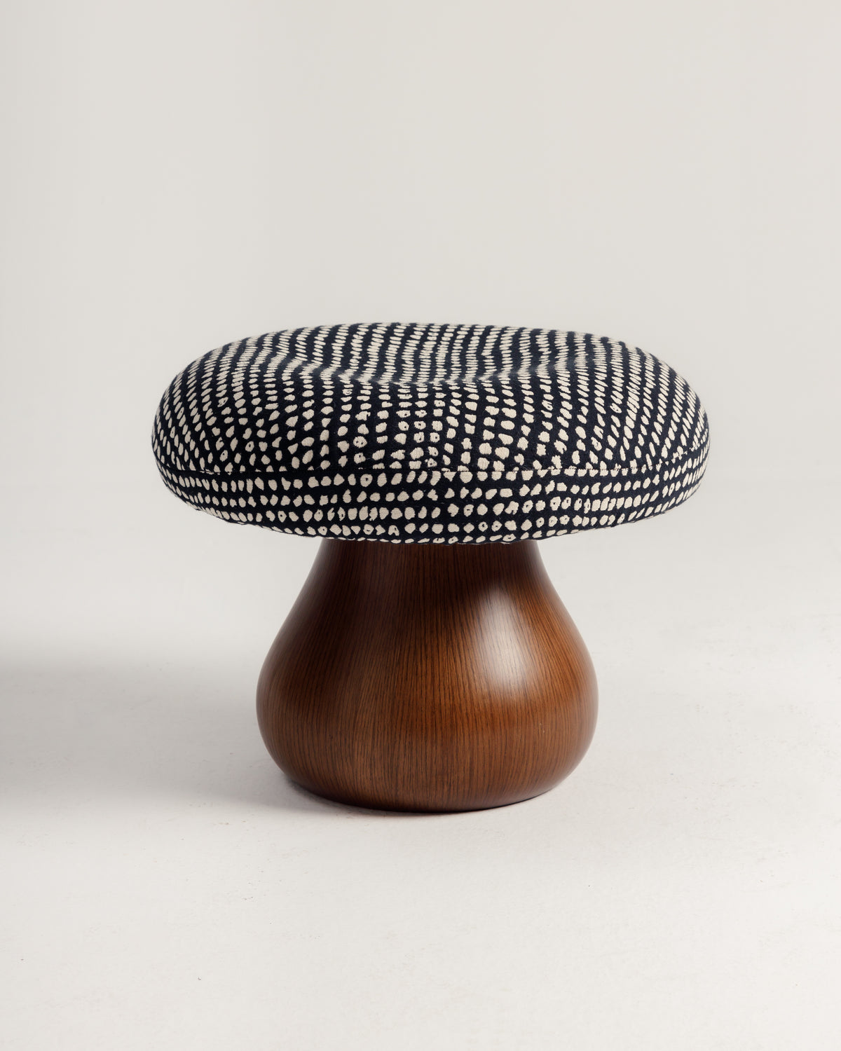 A stylish mushroom-shaped pouf featuring a curvaceous wooden base and a generously padded cushion with a black and white dotted pattern. This piece combines modern design with organic charm, making it a perfect accent for any living space.