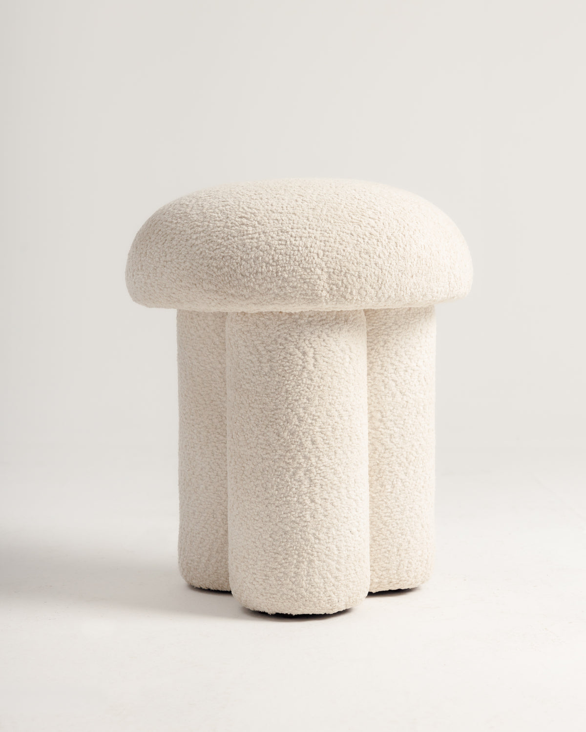 A modern, off-white pouf featuring a plush, domed top and a dual cylindrical base, wrapped in a soft bouclé fabric. The design is sculptural and contemporary, adding a cozy accent to any space.