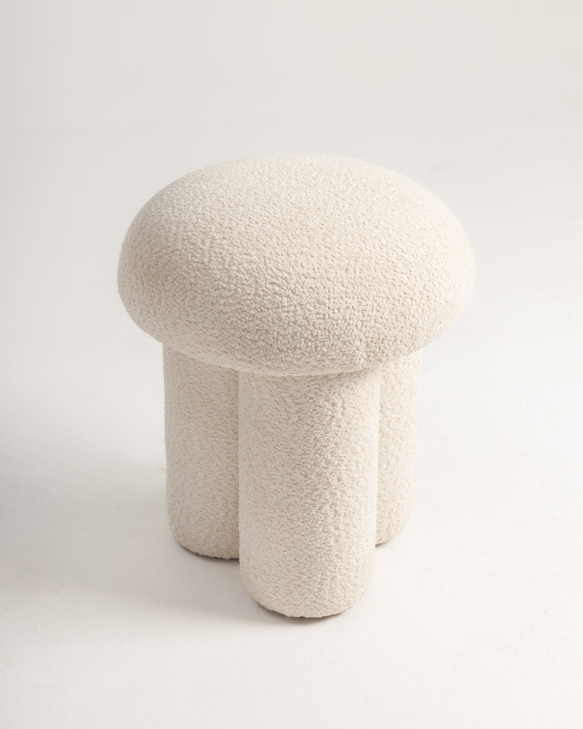 A soft, off-white pouf with a dual cylindrical base and a plush, rounded top, crafted from textured bouclé fabric. The modern design features a sculptural form, adding a cozy accent to any space.