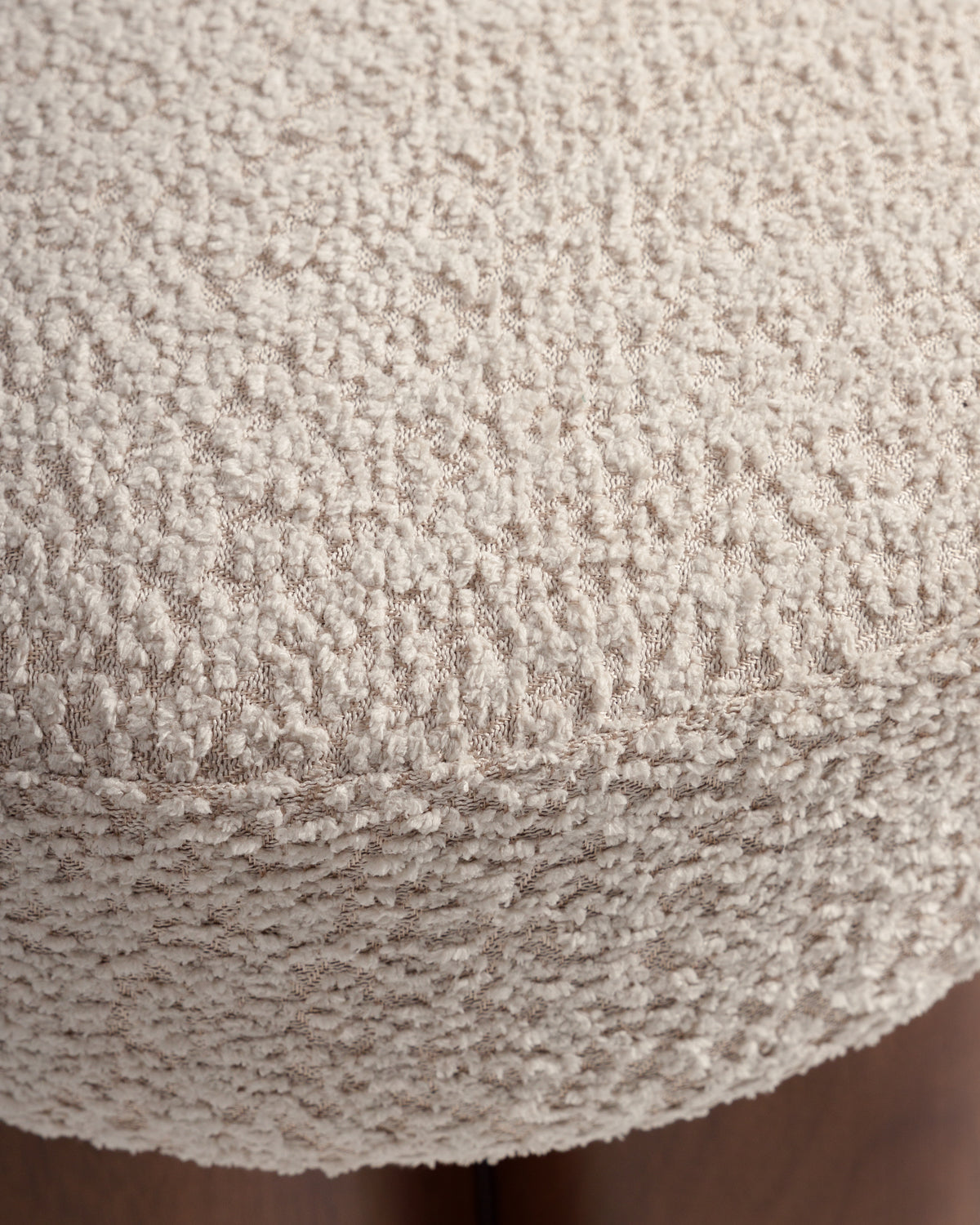 A close-up view of a textured cream cushion with a soft, plush surface. The cushion is part of a larger piece of furniture, featuring a round shape that appears comfortable and inviting.
