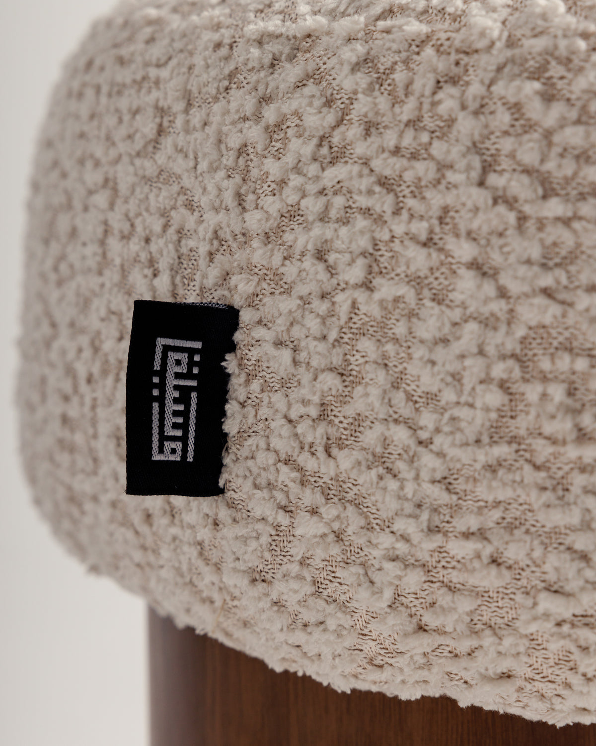 Close-up of a cozy cream cushion with a textured surface, resting on a wooden base. A small black label is visible on the cushion, adding a touch of detail to the overall design.